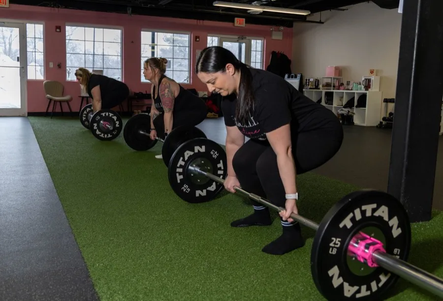 Women performing coached deadlifts in a row at Barbell Boutique