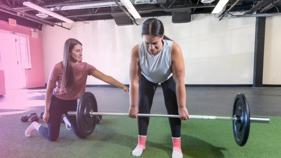 Coach spotting a client during a barbell deadlift